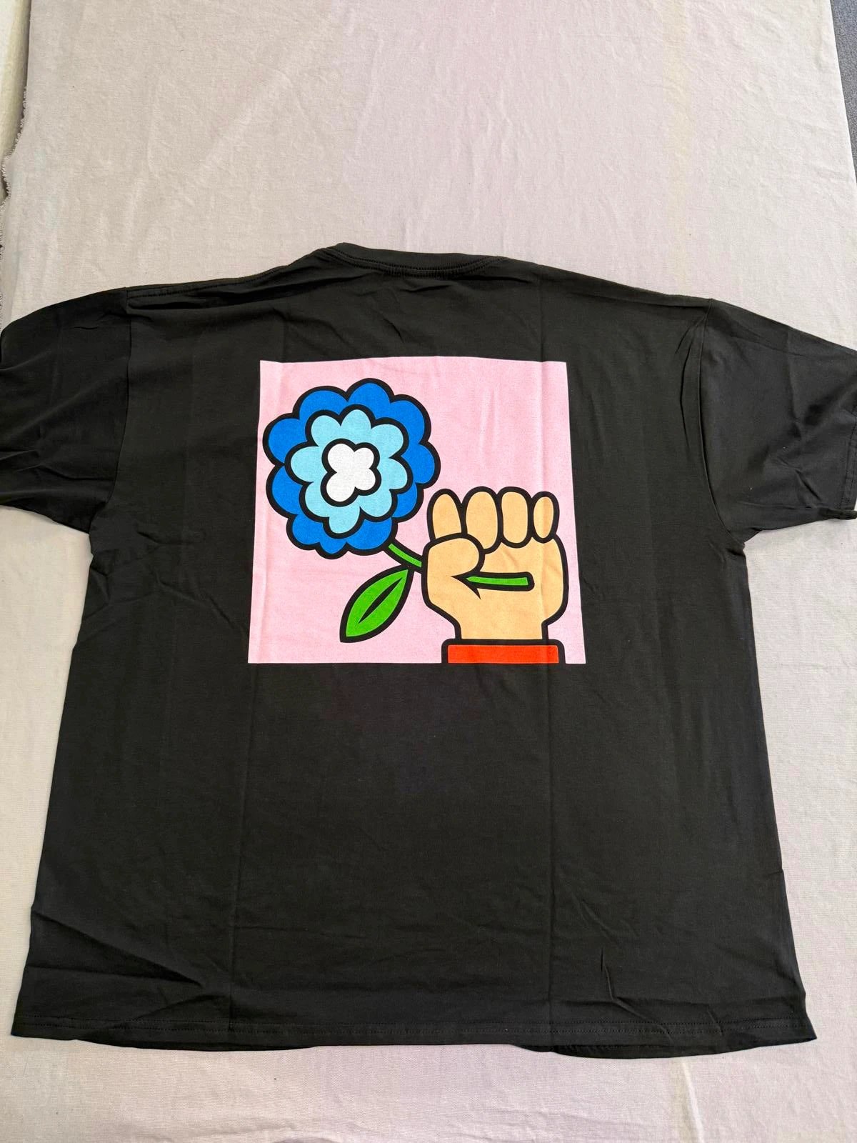 Black t-shirt with a colorful graphic of a flower and a fist on a light gray background