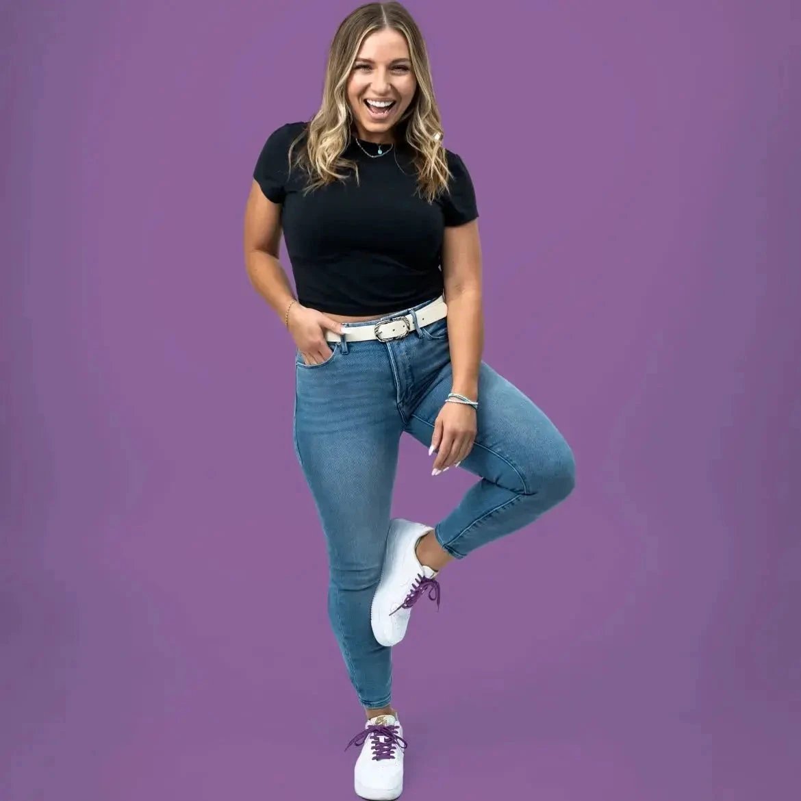 Woman wearing a black top and blue jeans against a purple background
