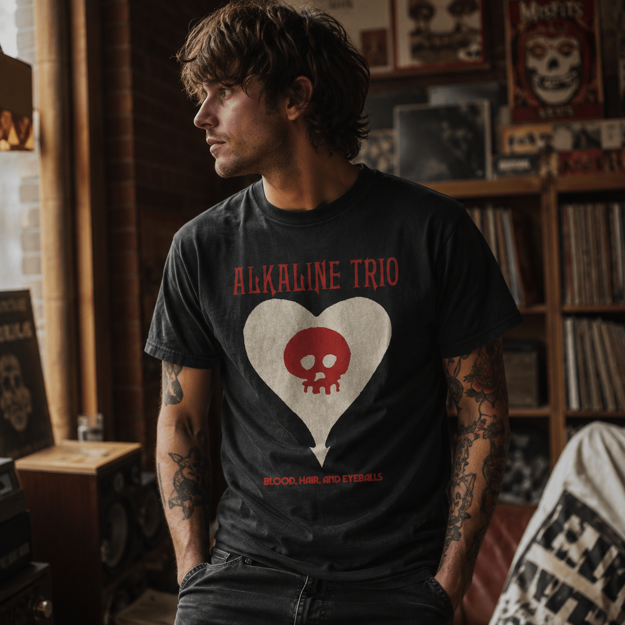 Male model wearing an Alkaline Trio Heartskull black t-shirt in a vintage music room with vinyl records and punk rock decor.