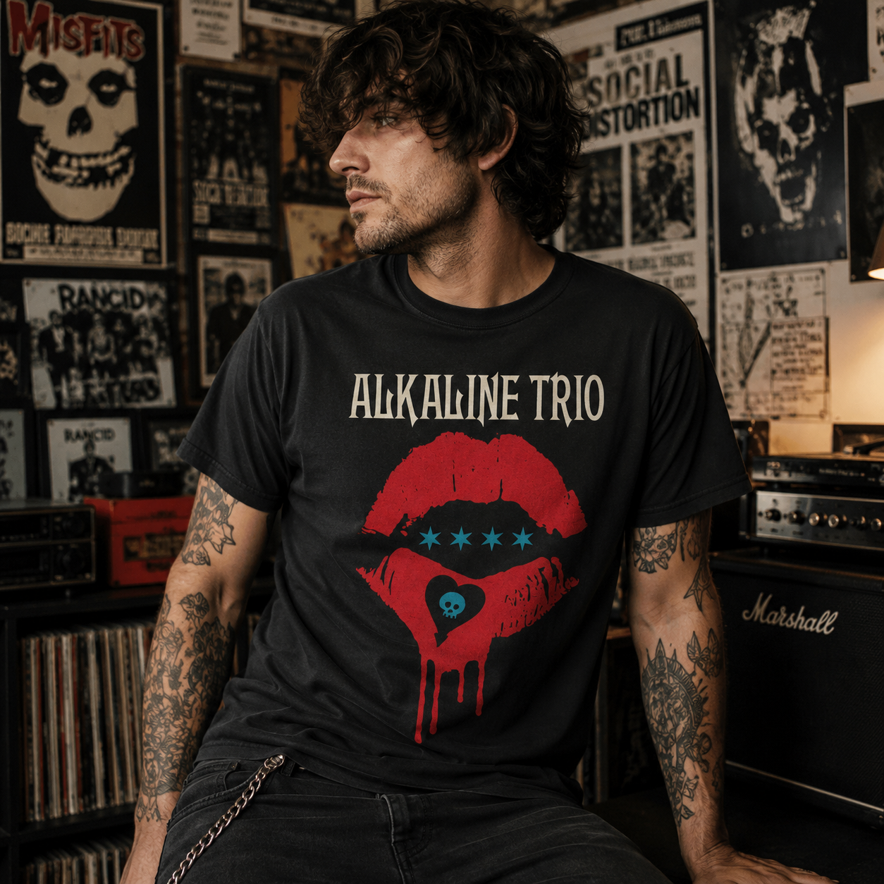 Male model wearing an Alkaline Trio Riot Fest Lips black t-shirt in a grungy punk rock room with posters, records, and guitar amps.