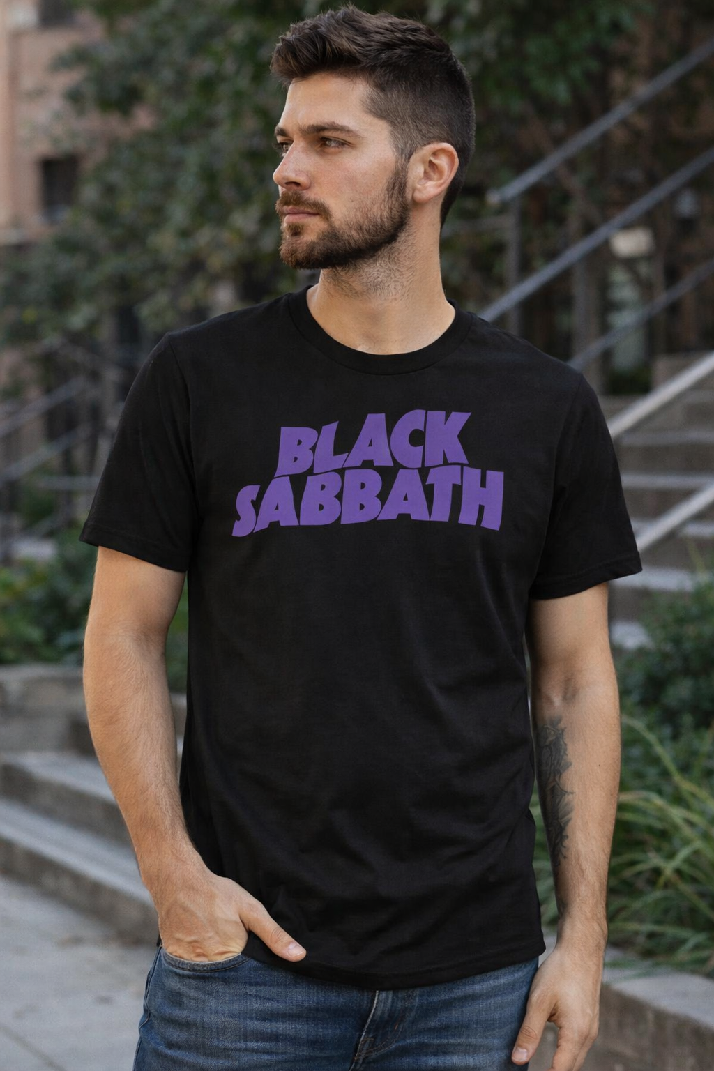 male model wearing Black Sabbath logo t-shirt with bold purple band text on black heavy metal tee in casual streetwear setting