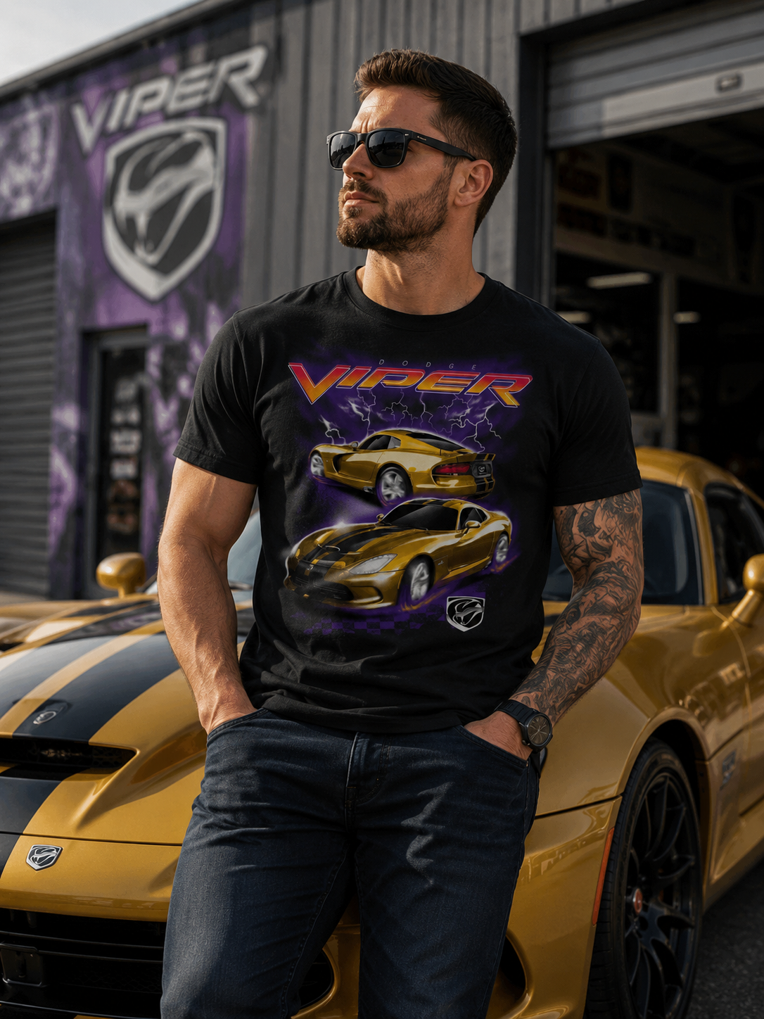 Male model wearing a Dodge Viper Storm graphic t-shirt standing in front of a gold Dodge Viper sports car outside a performance garage with Viper branding