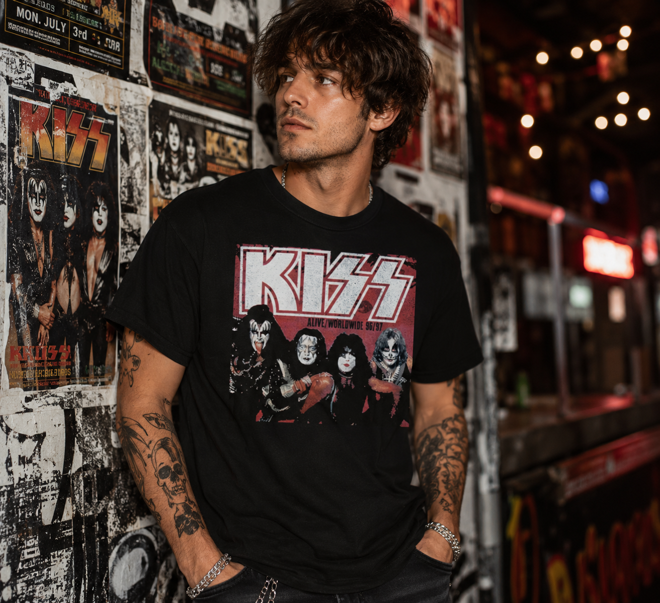 Male model wearing a KISS Alive Worldwide Tour black t-shirt in an urban nightlife setting with vintage concert posters, showcasing officially licensed KISS merchandise inspired by the legendary 96/97 reunion tour.