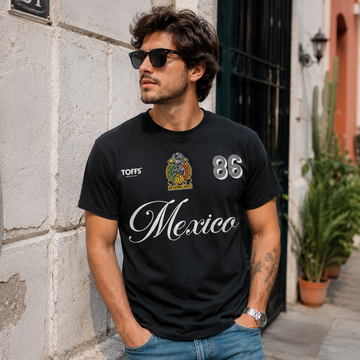 Male model wearing Mexico black retro soccer t-shirt with white script lettering, crest artwork, and number 86 futbol design