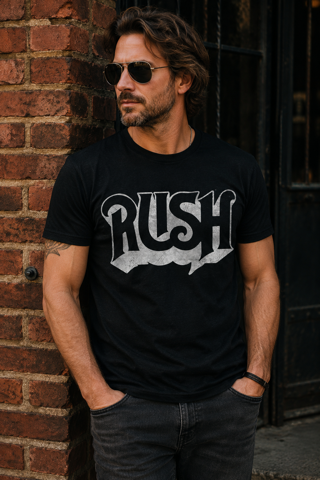 Male model wearing an officially licensed Rush black t-shirt featuring the distressed vintage Rush logo, standing against a brick wall in a casual rock-inspired lifestyle setting. Perfect for fans of classic progressive rock and band merchandise.