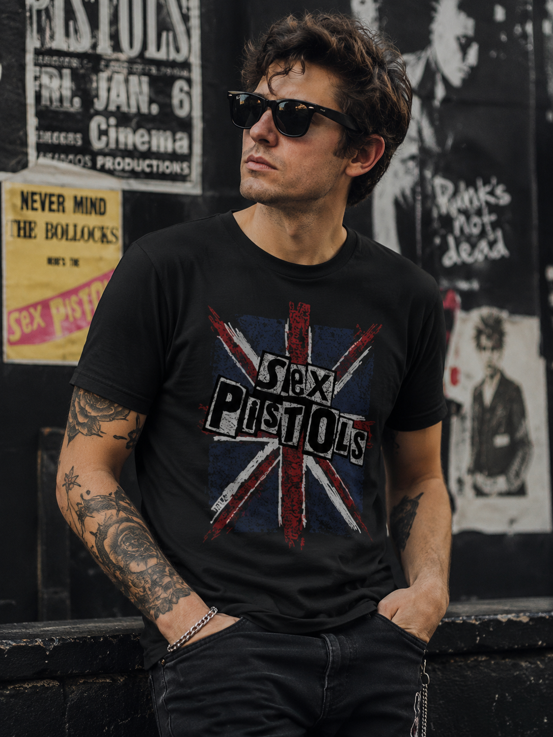 Male model wearing a Sex Pistols Union Jack T-Shirt in an urban punk-inspired street setting with vintage concert posters and graffiti backdrop