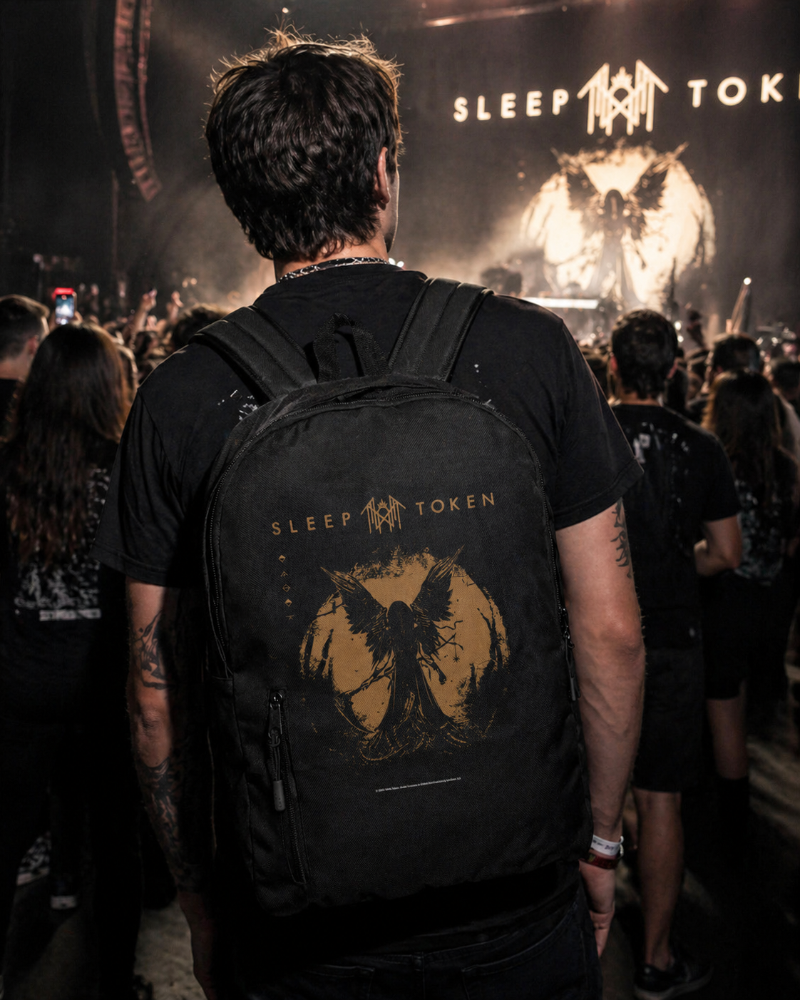 male model wearing Sleep Token TMBTE gold backpack at concert with crowd and stage lights in background