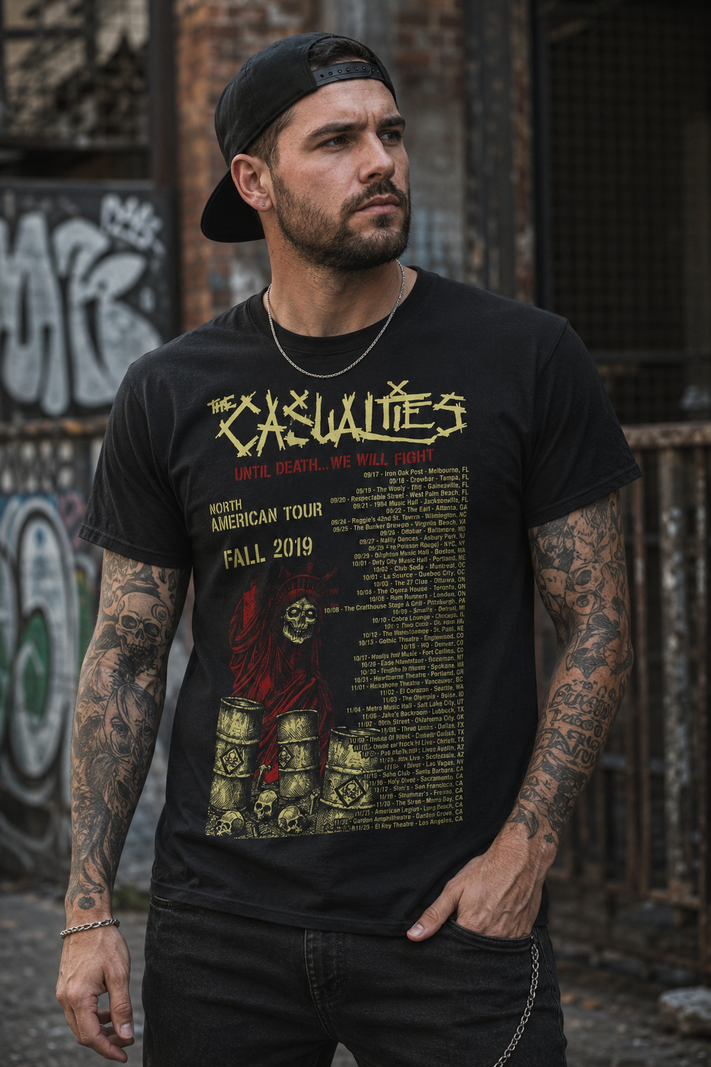 Male model wearing The Casualties Until Death North American Tour 2019 black t-shirt featuring official punk rock tour artwork in an urban streetwear setting.