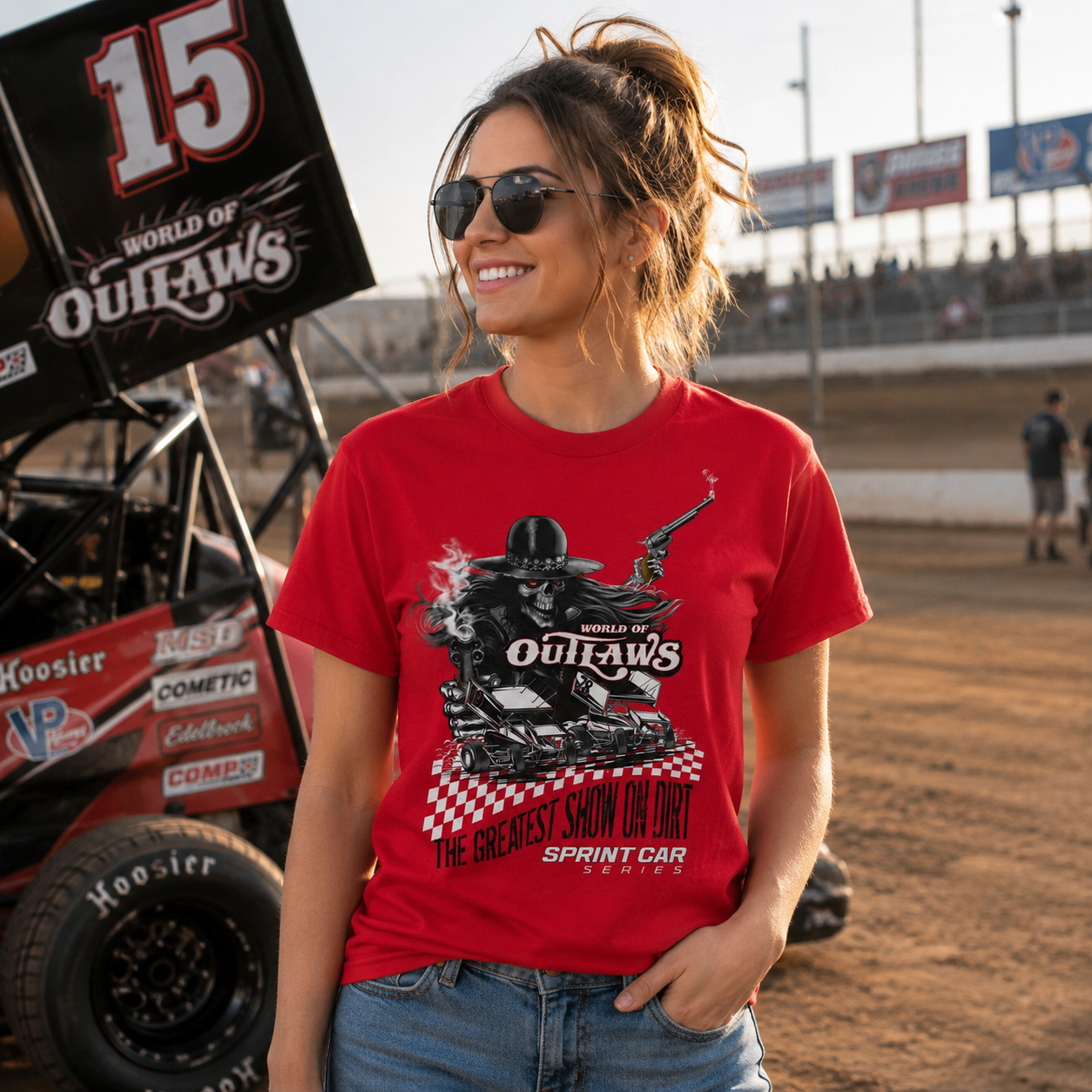 Female model wearing a World of Outlaws Greatest Show on Dirt red t-shirt at a dirt track raceway with a sprint car in the background