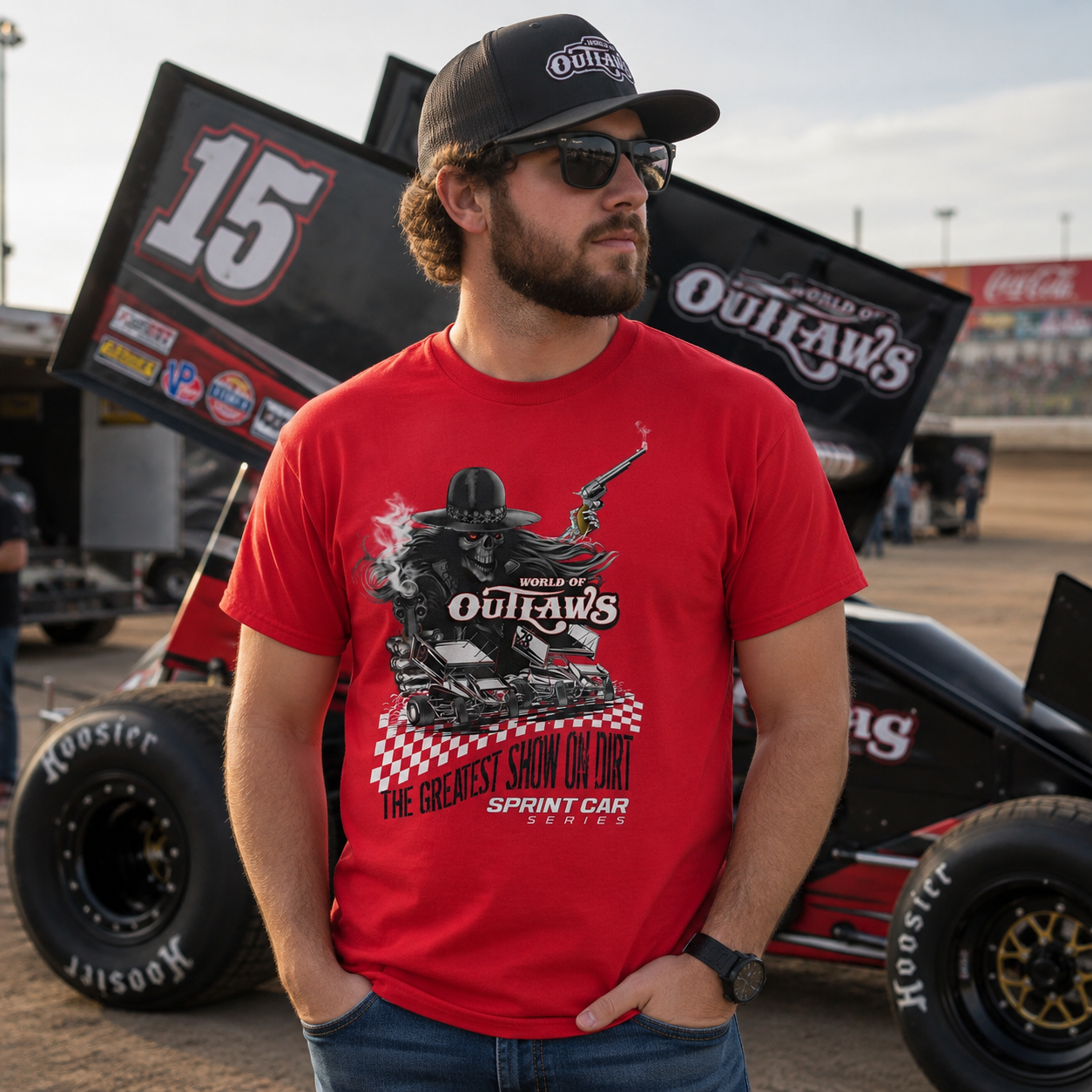 Male model wearing a World of Outlaws Greatest Show on Dirt red t-shirt standing beside a sprint car at a dirt track racing pit area