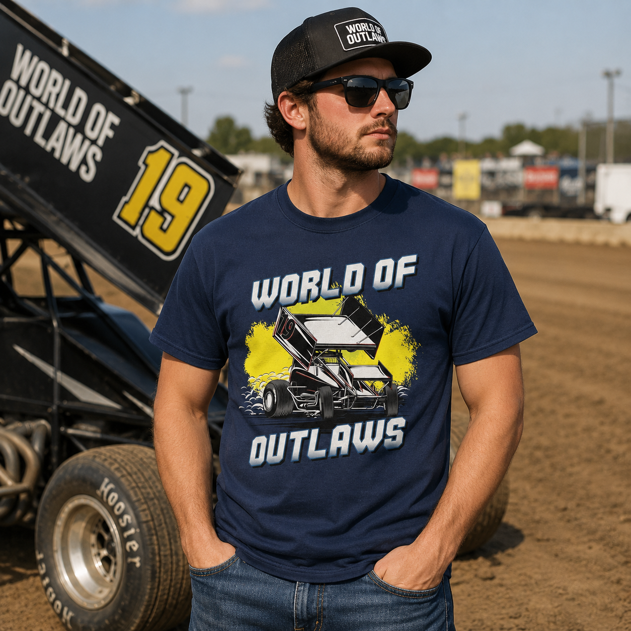 Male model wearing a World of Outlaws Yellow Splash Navy T-Shirt standing beside a sprint car at a dirt track racetrack during race day
